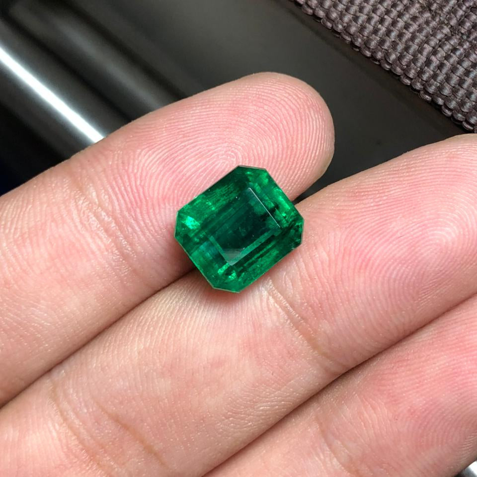 Green gemstone held between fingers against a blurred background