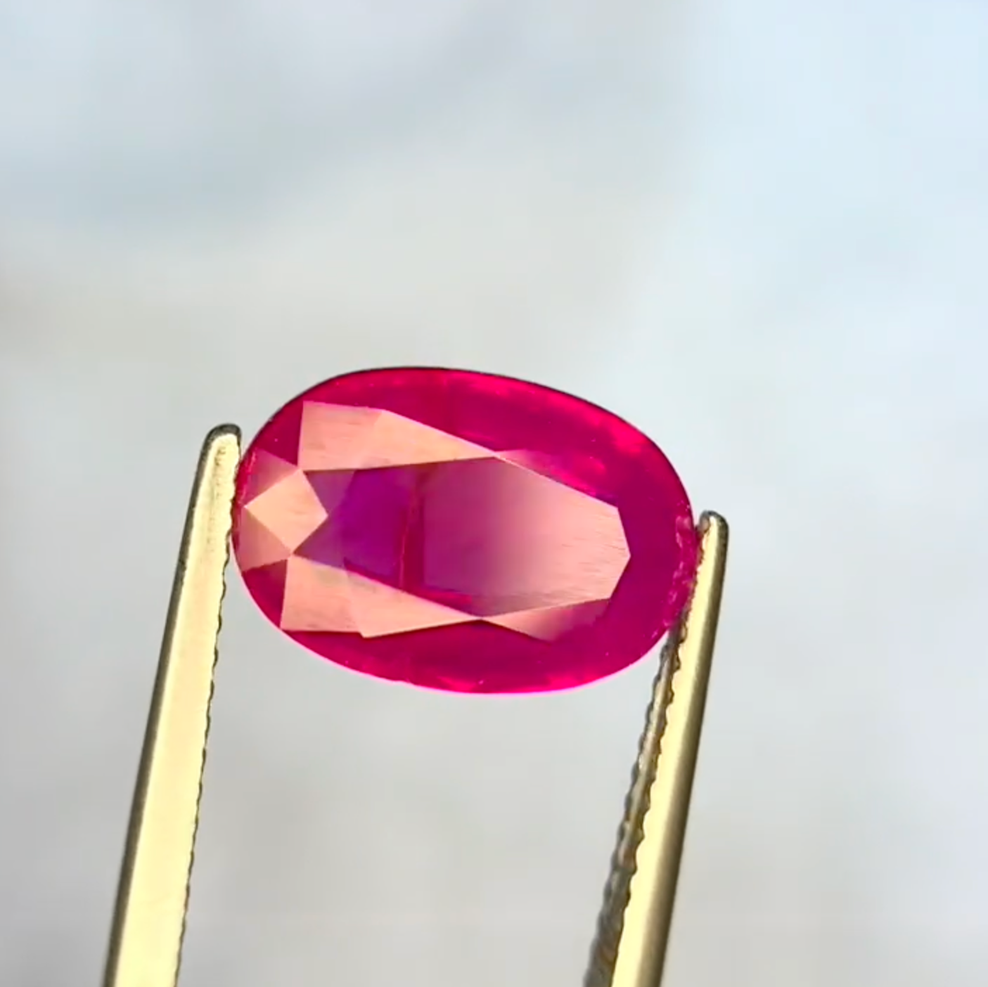 Ruby gemstone held between tweezers against a neutral background