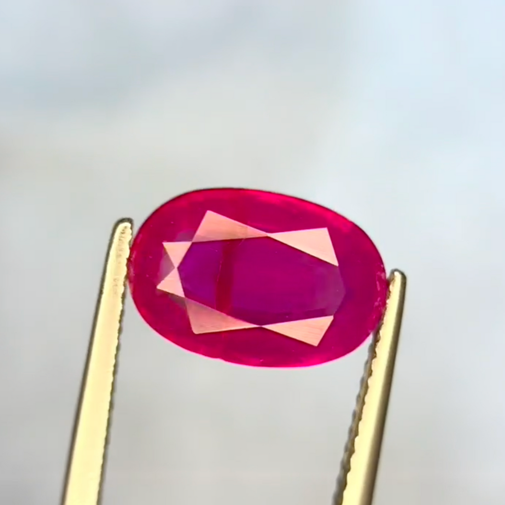 Oval-shaped pink gemstone held between tweezers against a light gray background