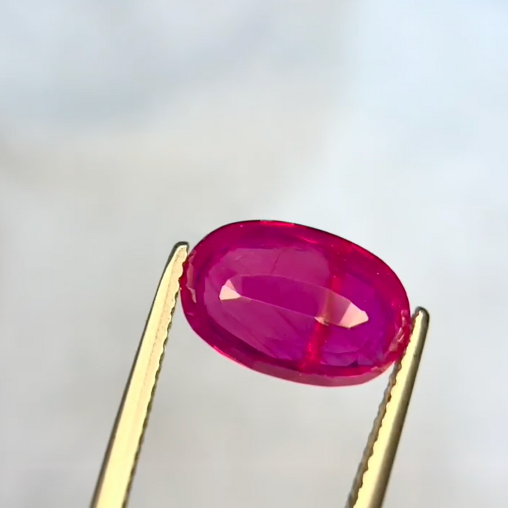 Oval-shaped pink gemstone held by tweezers against a light gray background