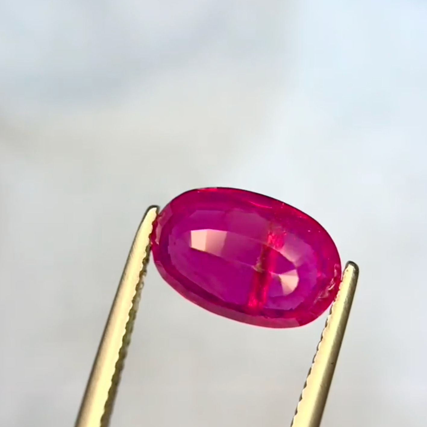 Oval-shaped red gemstone held by tweezers against a light gray background