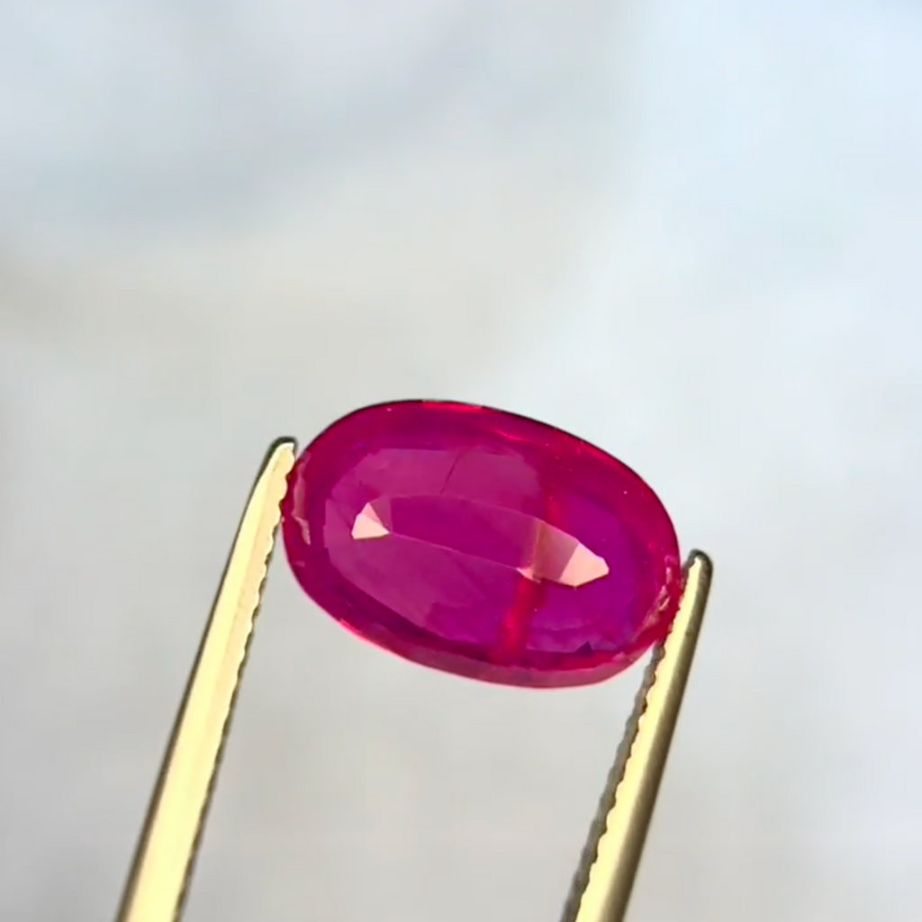 Oval-shaped ruby held by tweezers against a light gray background