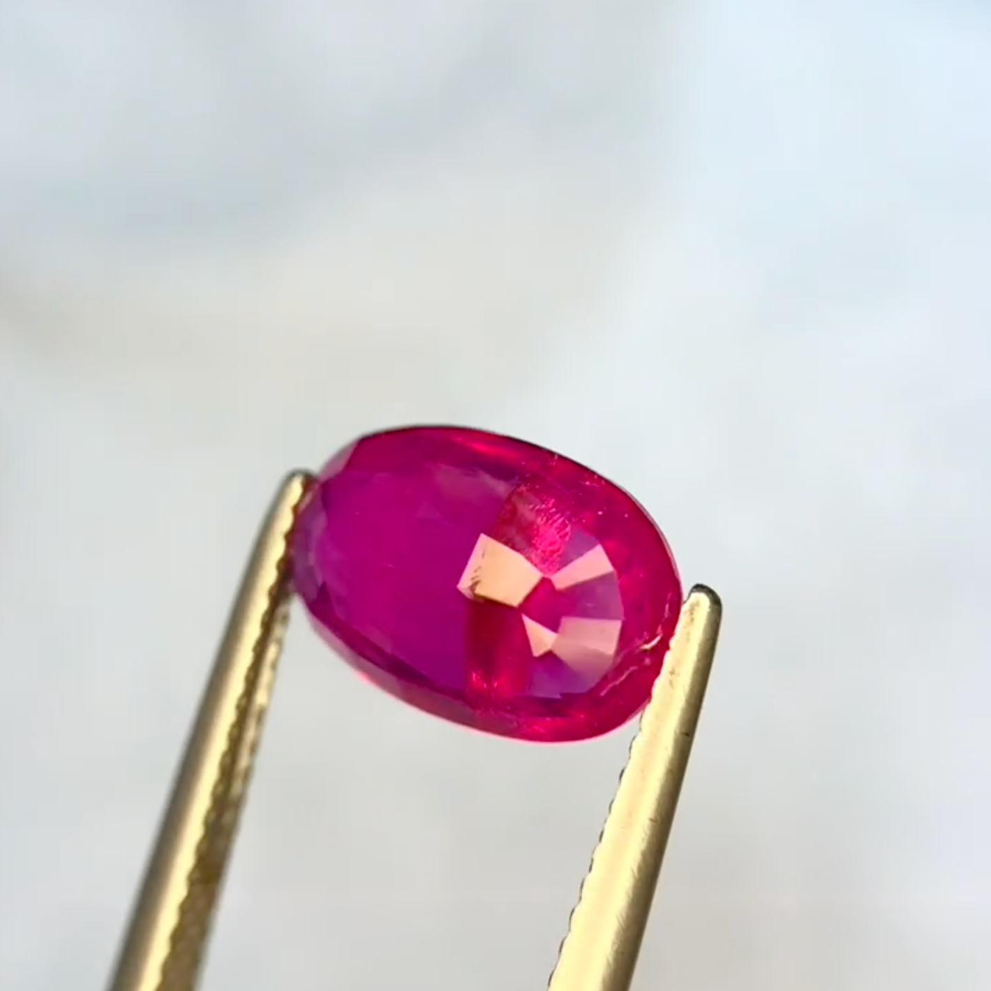 Oval-shaped pink gemstone held between two gold prongs against a white background