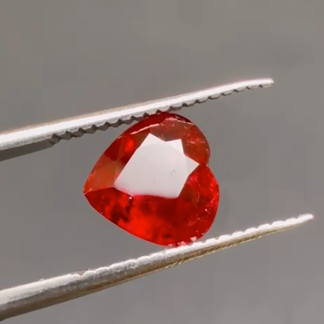Red gemstone held between tweezers against a neutral background