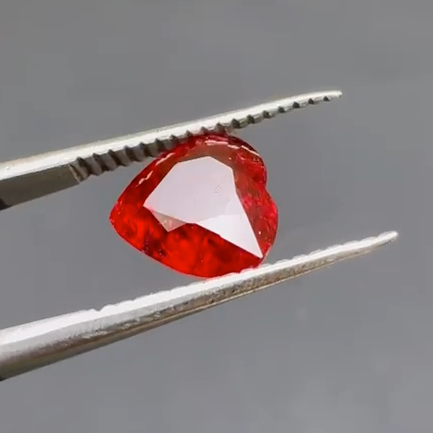 Red gemstone held between tweezers against a gray background