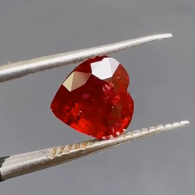Red gemstone held between tweezers against a gray background