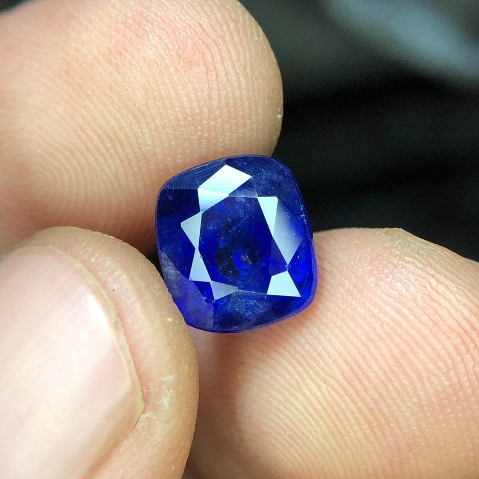 Blue gemstone held between two fingers against a blurred background