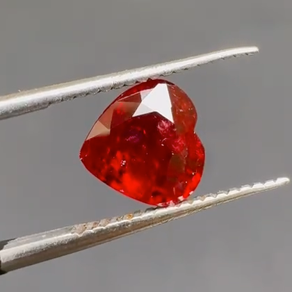Red gemstone held between tweezers against a gray background