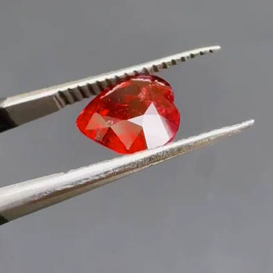 Red gemstone held between tweezers against a gray background